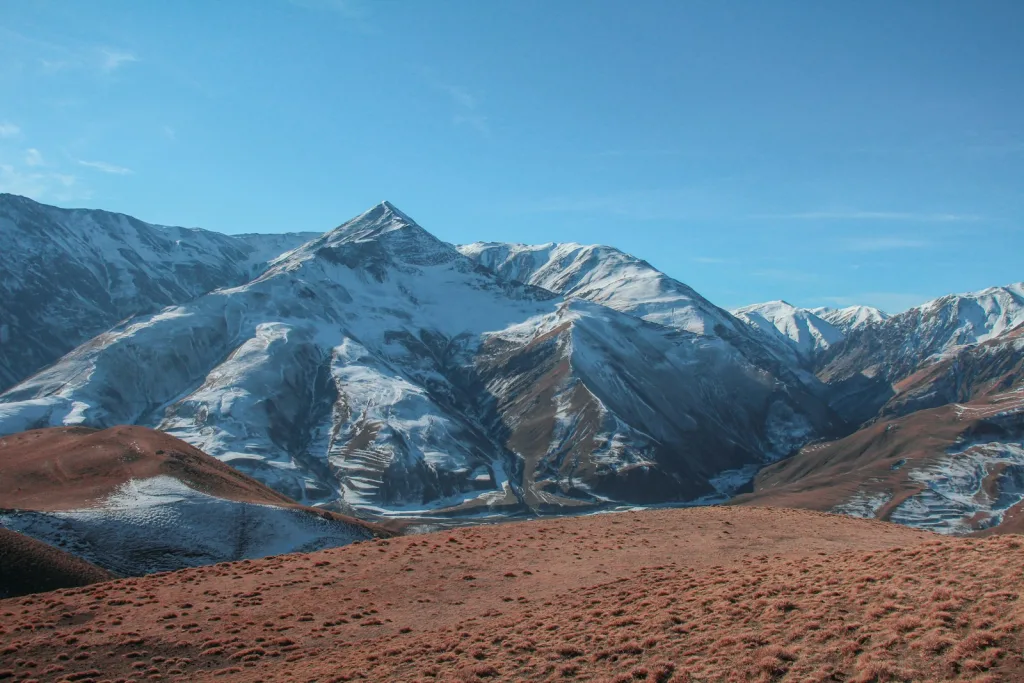 a view of a snowy mountain range from the top of a hill