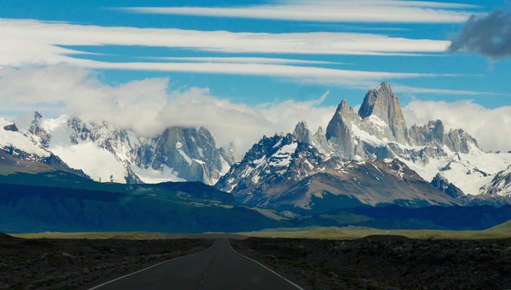 snow-covered mountain behind gray asphalt road