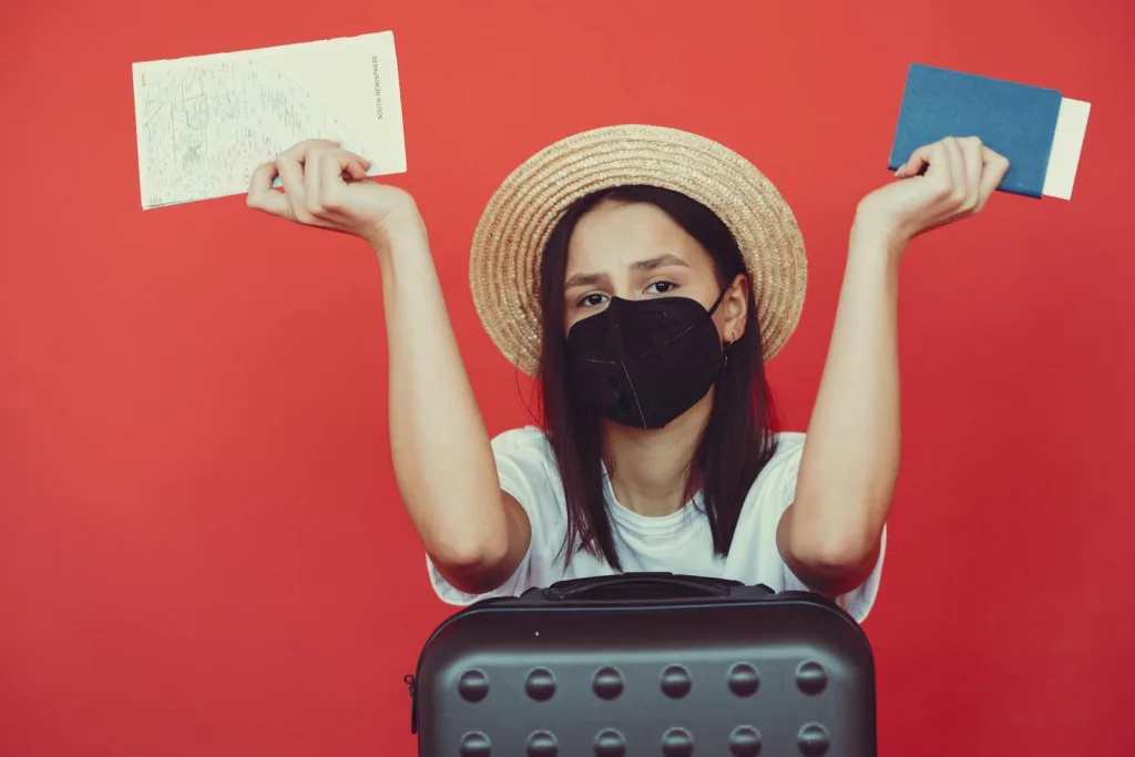 Sad woman in respiratory mask with suitcase and passport